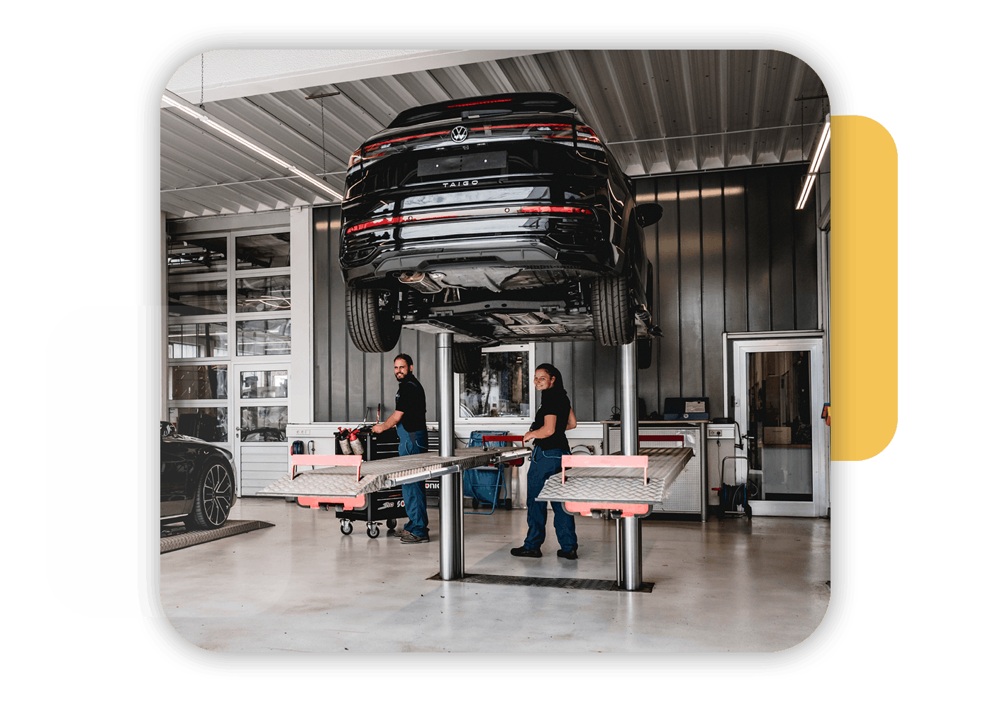 zwei Mitarbeiter in der VW Werkstatt, ein Auto steht auf einer Hebbühne